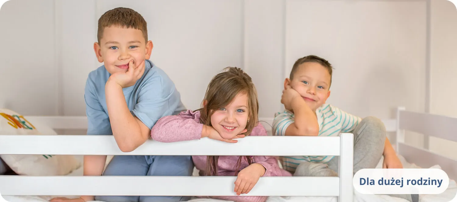 Troje uśmiechniętych dzieci opierających się o białą barierkę łóżka.